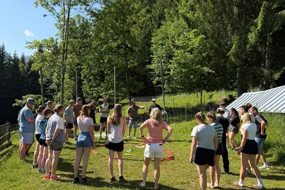 Eine Gruppe von Auszubildenden der Geiger Gruppe, welche bei strahlend blauem Himmel um ein rotes Band in der Mitte stehen.
