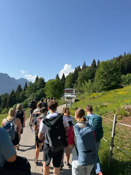 Eine Gruppe Auszubildenden auf einem Wanderweg zu einer Hütte.