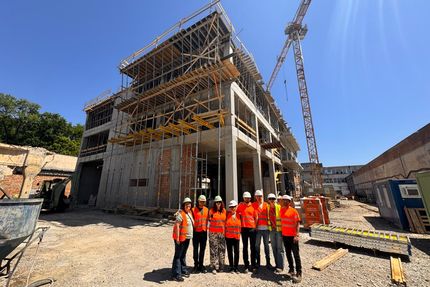 Eine Gruppe an Menschen vor einer Baustelle in Rumänien. Alle Personen auf dem Bild tragen eine orangene Warnweste und einen Helm.