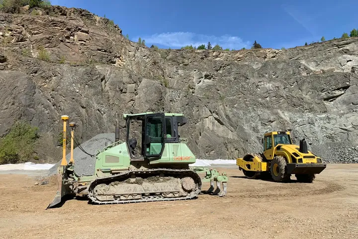 Planierraupe und gelbe Walze auf einer Erdfläche im Steinbruch – moderne Baumaschinen mit präziser Maschinensteuerung und digitaler Vermessung im Einsatz.