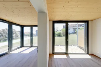 Zwei helle mit Licht durchflutete Räume mit Holzboden und Holzdecke, der Blick in den begrünten Garten.