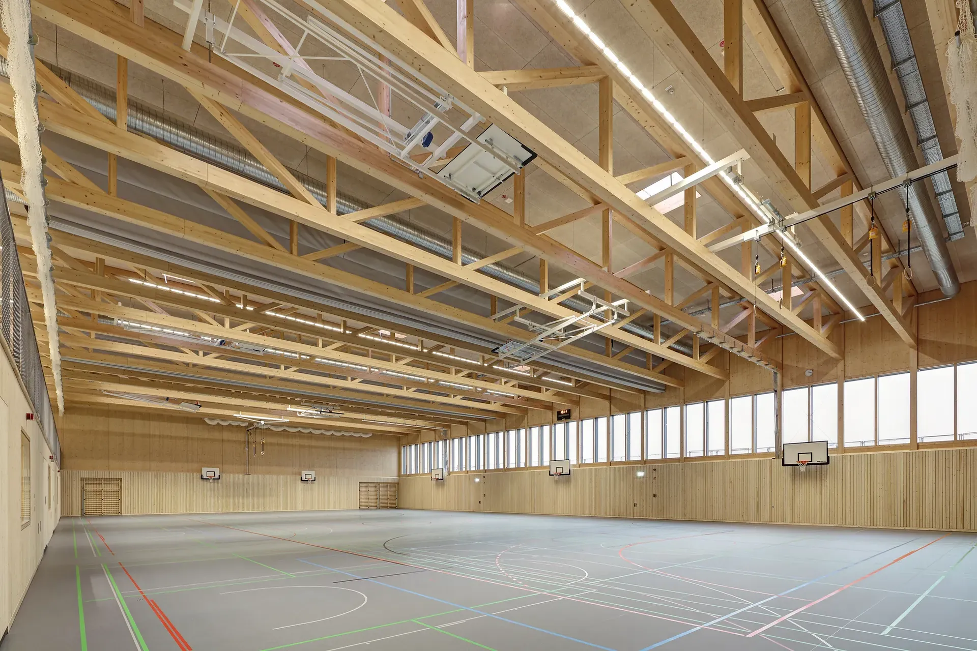 Blick in eine Sporthalle mit hohen Decken, Bodenzeichnungen und Holzelementen.