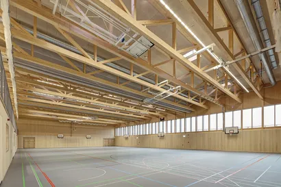 Blick in eine Sporthalle mit hohen Decken, Bodenzeichnungen und Holzelementen.