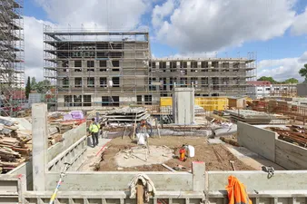 Eine Baugrube mit unterschiedlichen Materialien für den Neubau des Quartier am Rotweg, im Hintergrund ein Haus im Gerüst.
