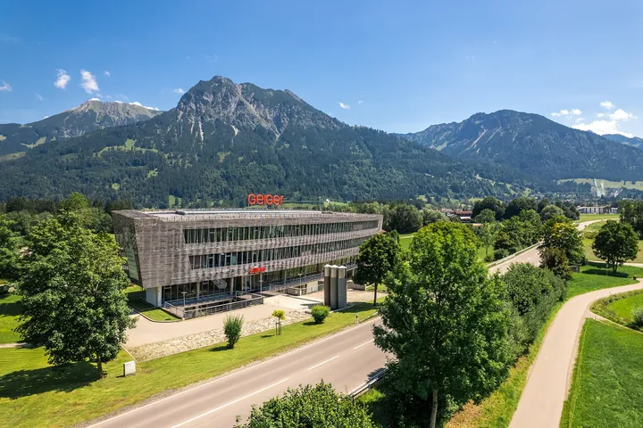 Luftaufnahme der Hauptzentrale der Geiger Gruppe in Oberstdorf, eingebettet in eine Landschaft mit grünen Wiesen und Bergen im Hintergrund.