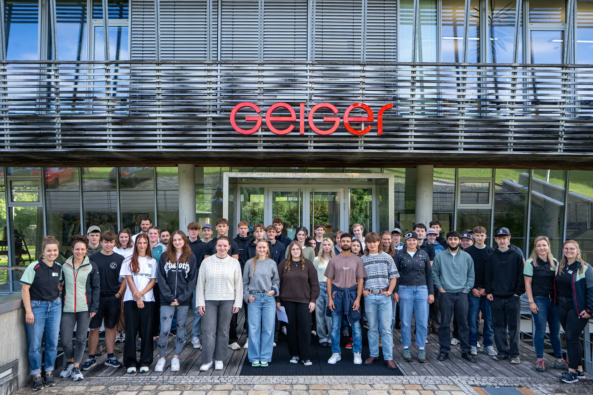 Eine Gruppe von Menschen steht vor einem Gebäude, über dessen Eingang „Geiger“ steht.