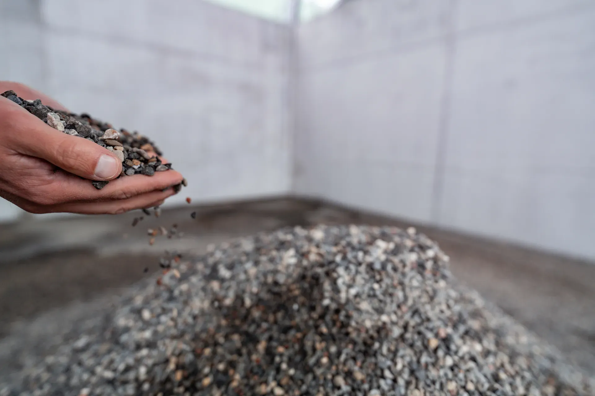 Eine Hand, in der sich Kies befindet und ein Kieshaufen im Hintergrund.