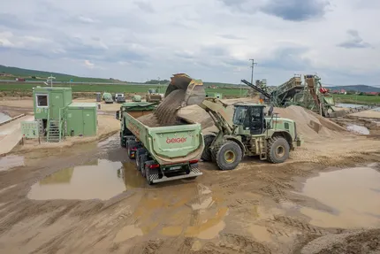 Ein Radlader kippt Kies auf einen Lkw. Im Hintergrund ein Kieswerk in Rumänien.
