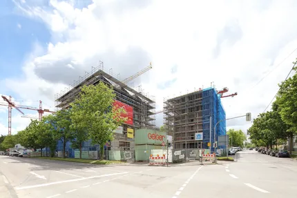 Zwei Gebäude eingehüllt in Gerüsten, im Hintergrund Krane.