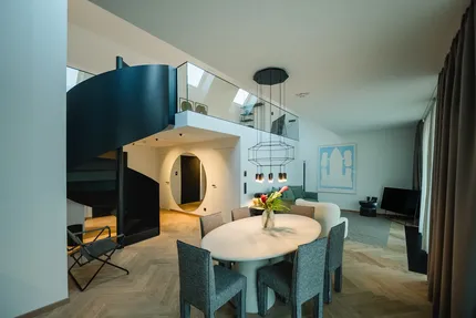 Wohn- und Essbereich mit schwarzer Wendeltreppe und Gallerie. Im Vordergrund ein moderner Esstisch.