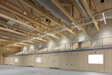 Eine Sporthalle mit hohen Decken und Holzelementen an den Wänden - im Hintergrund eine Zuschauertribüne.