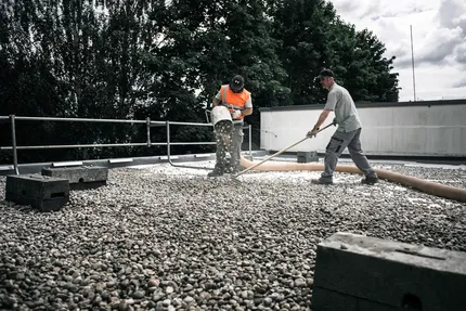 Zwei Männer bekiesen ein Flachdach mit einem modernen Saugbagger.