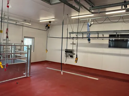 Eine große Halle mit rotem Boden. Von der Decke hängen Steckdosen und vreschiedene Ketten.