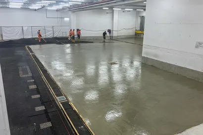 Arbeiter in Sicherheitskleidung glätten und ebnen frisch gegossenen Beton auf einem großen Boden im Innenbereich.