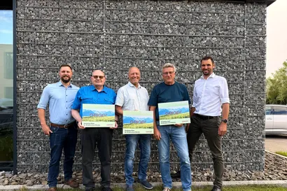 Die Gesellschafter stehen mit den drei in Rente verabschiedeten Mitarbeitenden vor einer Steinwand. Die Neurentner in der Mitte halten alle ein Bild auf Leinwand in der Hand.