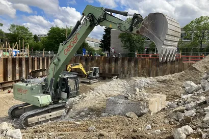 Ein grüner Bagger mit roter Aufschrift "Geiger" in einer Baugrube.