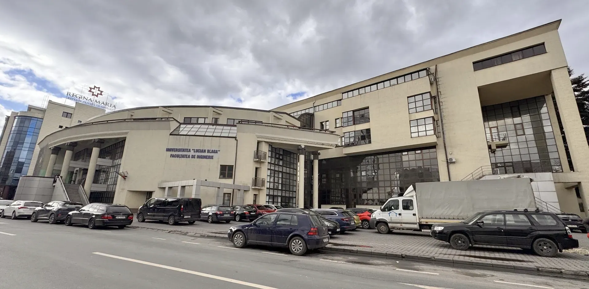 Clădire mare, bej, cu ferestre din sticlă, etichetată „Centrul de Tineret Belgrad”, sub un cer înnorat. Mașinile parcate aliniază strada din față.