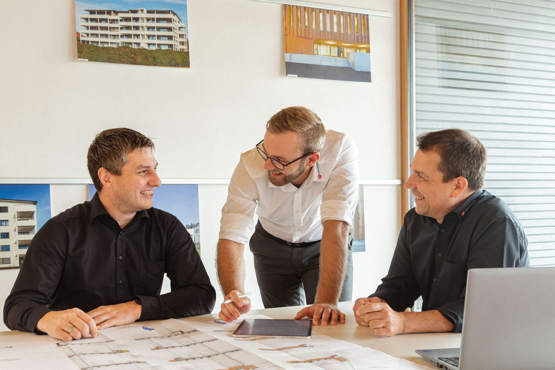 Zwei Mitarbeiter und ein Kunde besprechen Holzbaupläne im Büro.