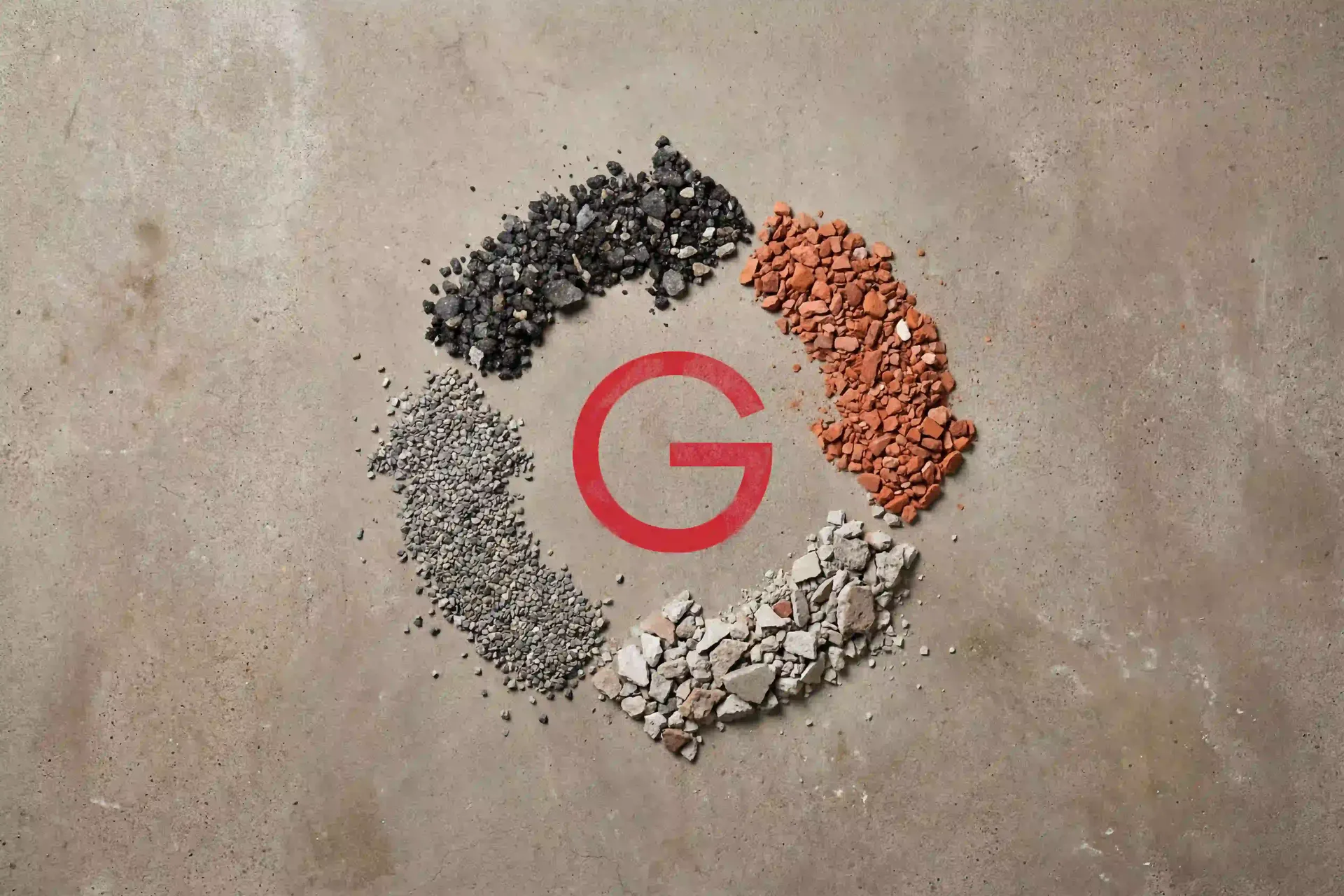 Ein rotes ‚G‘ ist von schwarzen, roten, grauen und weißen Kieshaufen umgeben, die kreisförmig auf einem Betonuntergrund angeordnet sind.