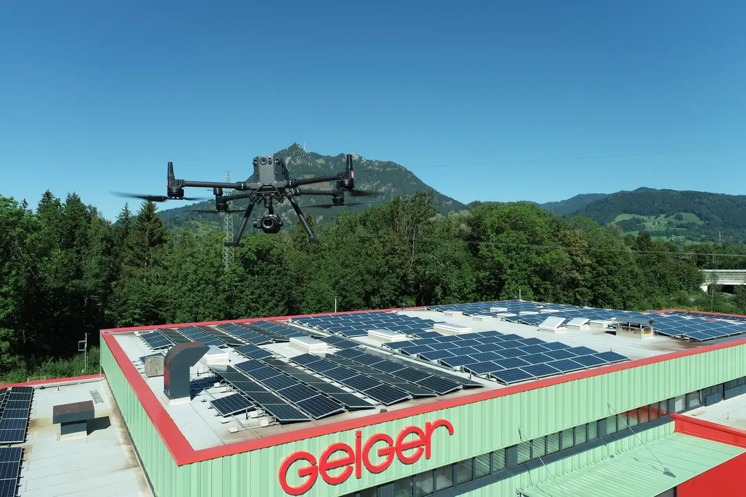 Drohne bei der Vermessung eines Gebäudes mit Solaranlagen in bergiger Landschaft. Drohne‑Vermessung aus der Luft