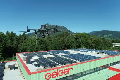Drohne bei der Vermessung eines Gebäudes mit Solaranlagen in bergiger Landschaft. Drohne‑Vermessung aus der Luft