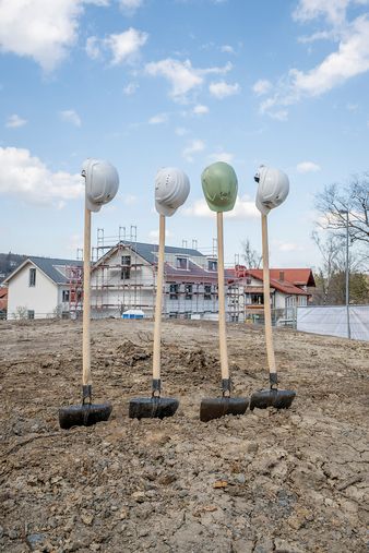 "Vier Schaufeln mit Helm stecken symbolisch beim Spatenstich in der Erde"