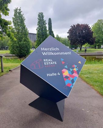 Ein Aufsteller mit der Aufschrift "Herzlich Willkommen" in Form eines Würfels vor dem Messegelände.