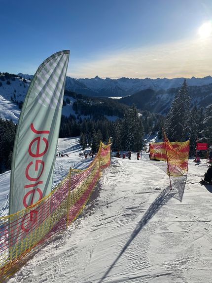 Blick auf die verschneite Skipiste beim Geiger Cup 2025 mit Geiger-Banner und spektakulärer Alpenkulisse im Hintergrund