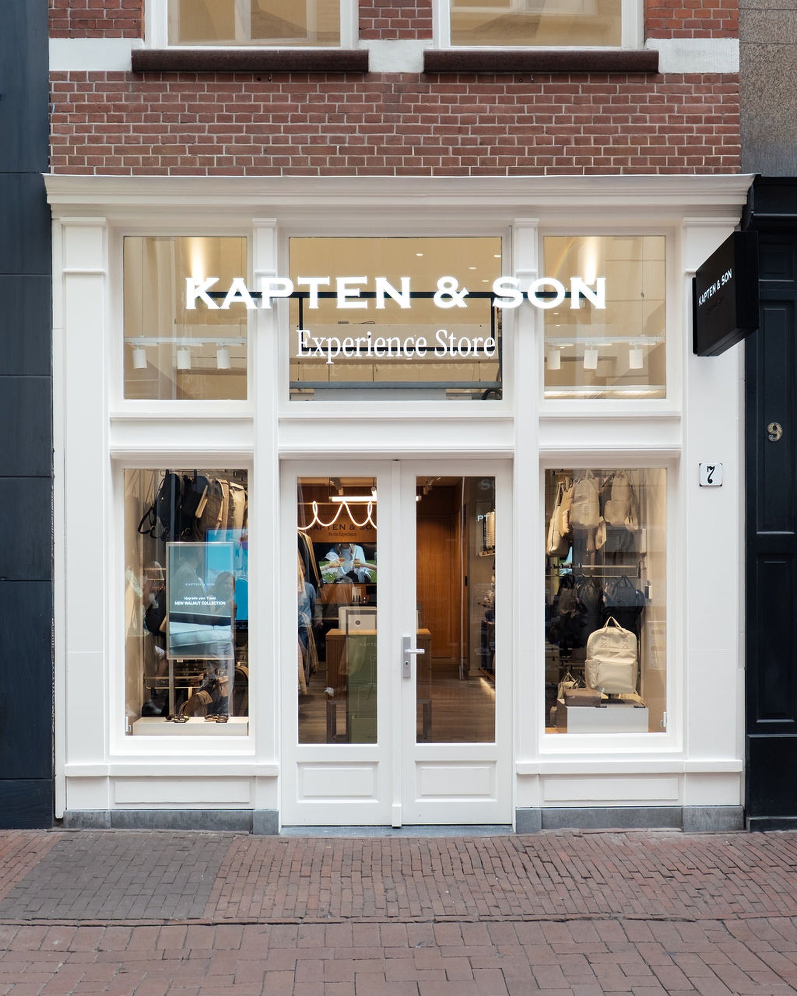 Kapten & Son Experience Store – Ladenfront mit beleuchtetem Logo, Rucksäcken, Taschen und Reisegepäck in den Schaufenstern