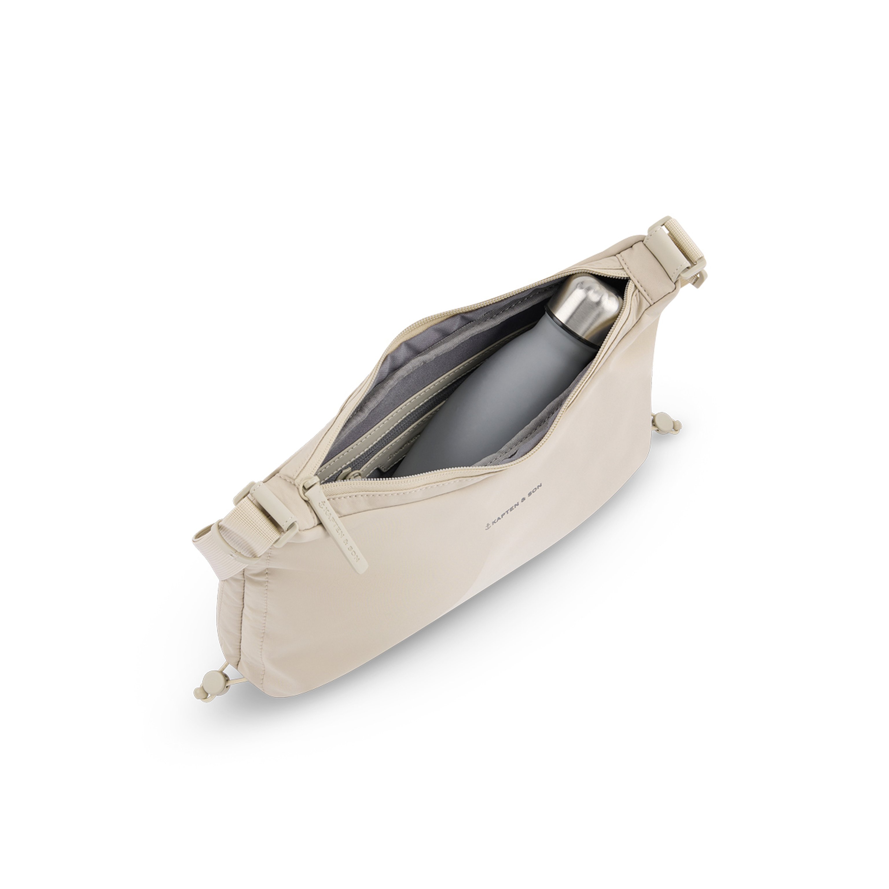 Beige crossbody bag with open zipper, containing a metallic grey water bottle. The bag has adjustable straps and a minimalist design.