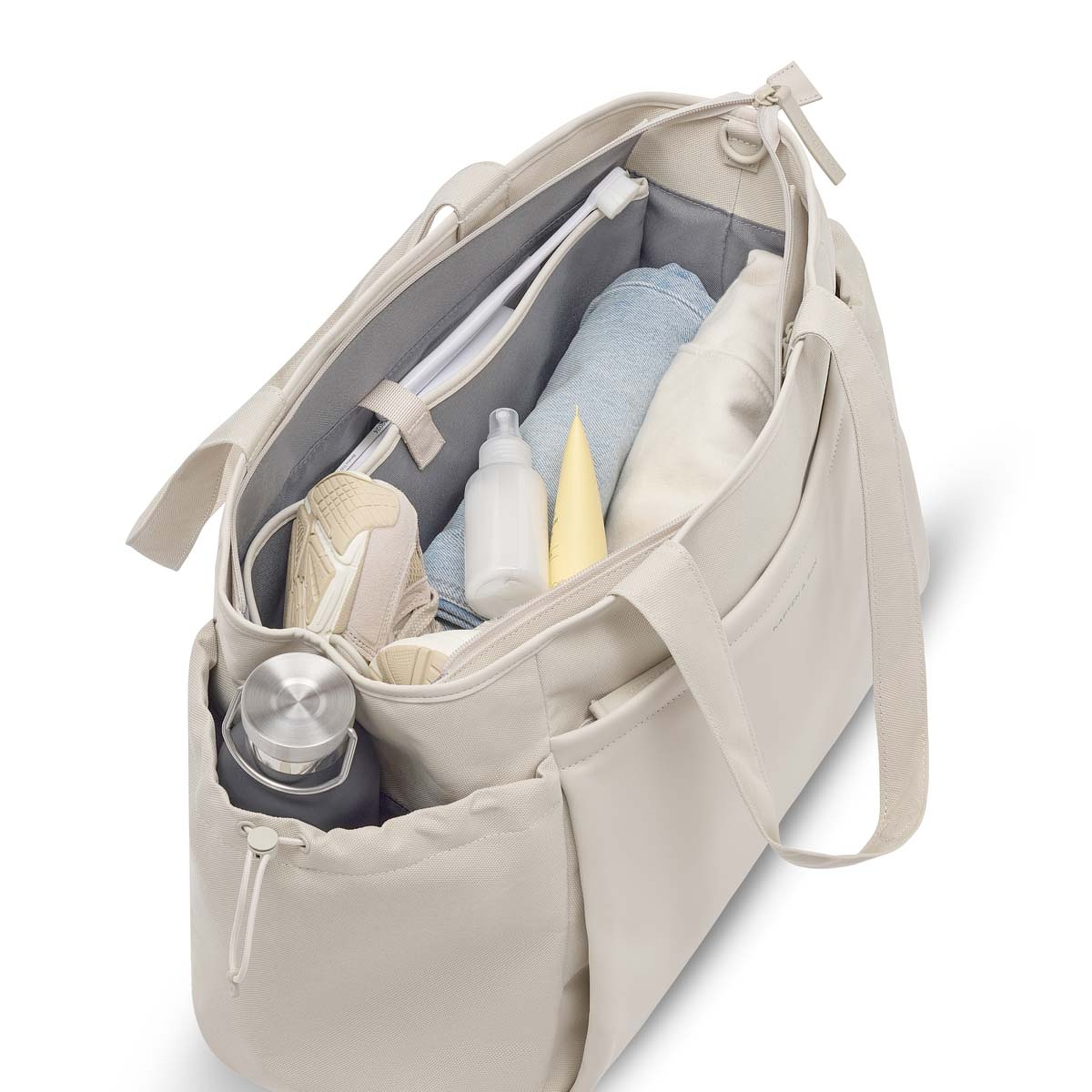 Offene beige Sporttasche, gefüllt mit Sneakers, Handtuch, Trinkflasche und Pflegeartikeln, übersichtlich im Innenraum sortiert.