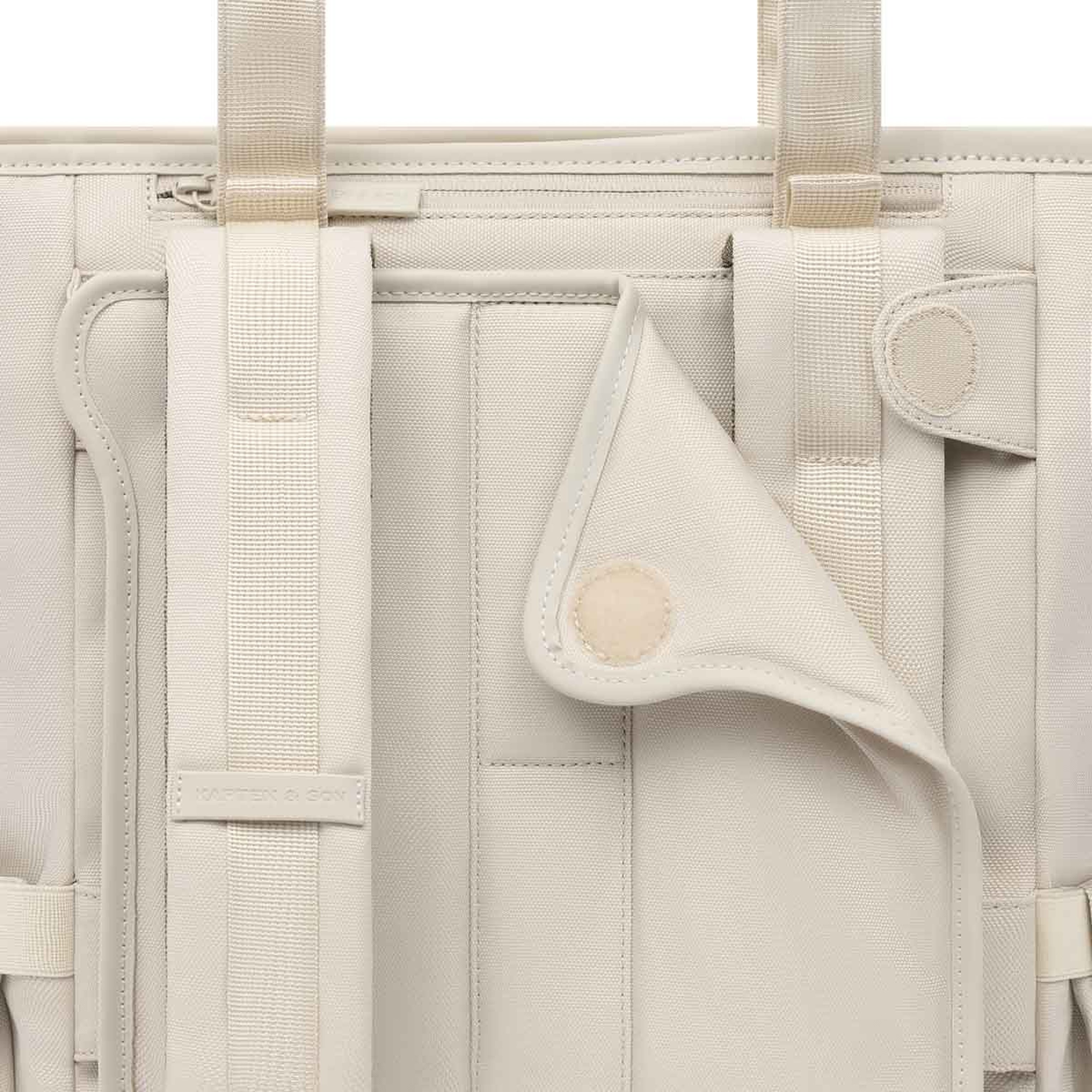 Nahaufnahme eines beigen Rucksack aus Stoff mit Riemen und Klappe mit Knopfverschluss. Die Textur ist weich und minimalistisch.