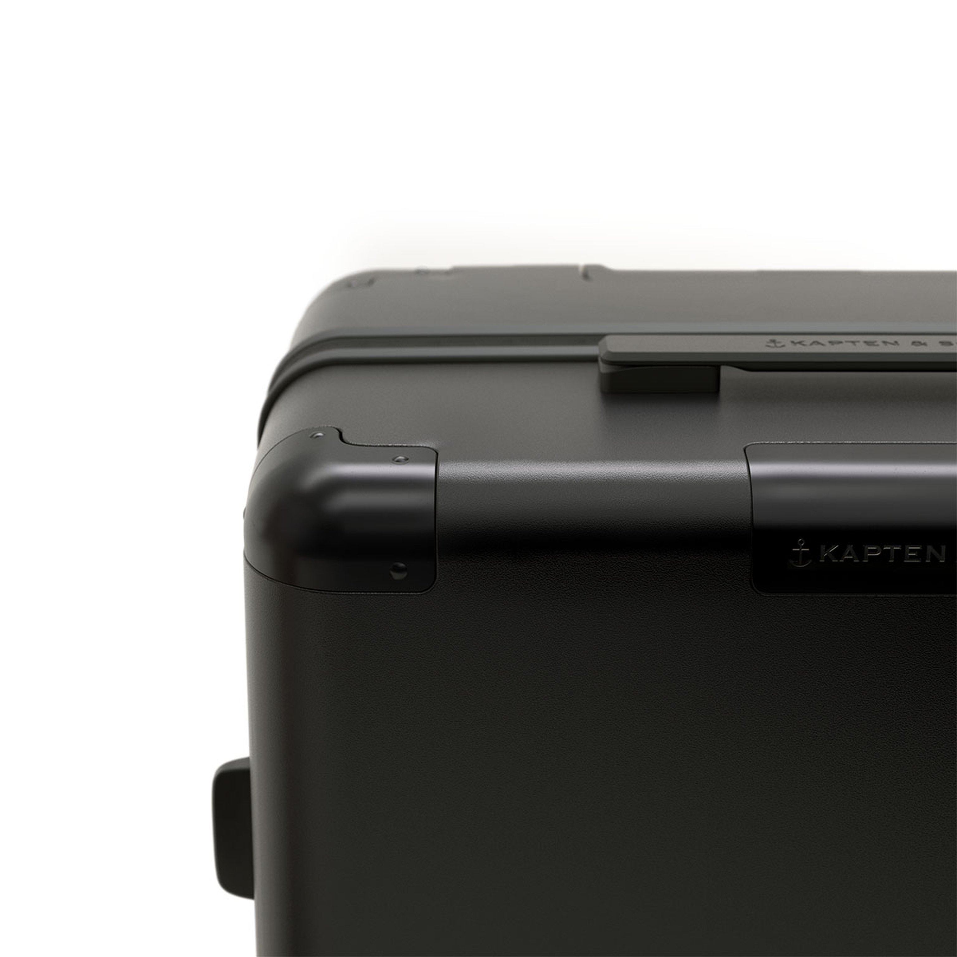 Close-up of a sleek black suitcase corner with smooth curves and a handle. The modern, minimalist design conveys durability and quality.