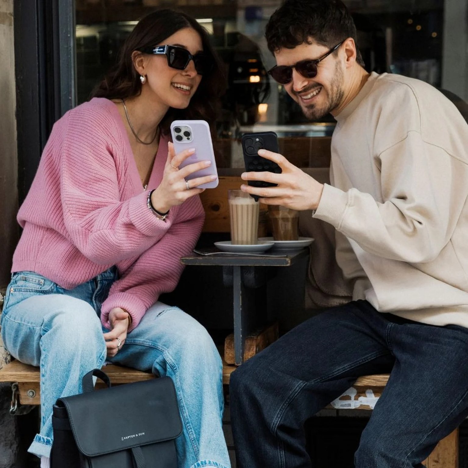 Zwei junge menschen sitzen im kaffee und schauen lächelnd auf ihr smartphone