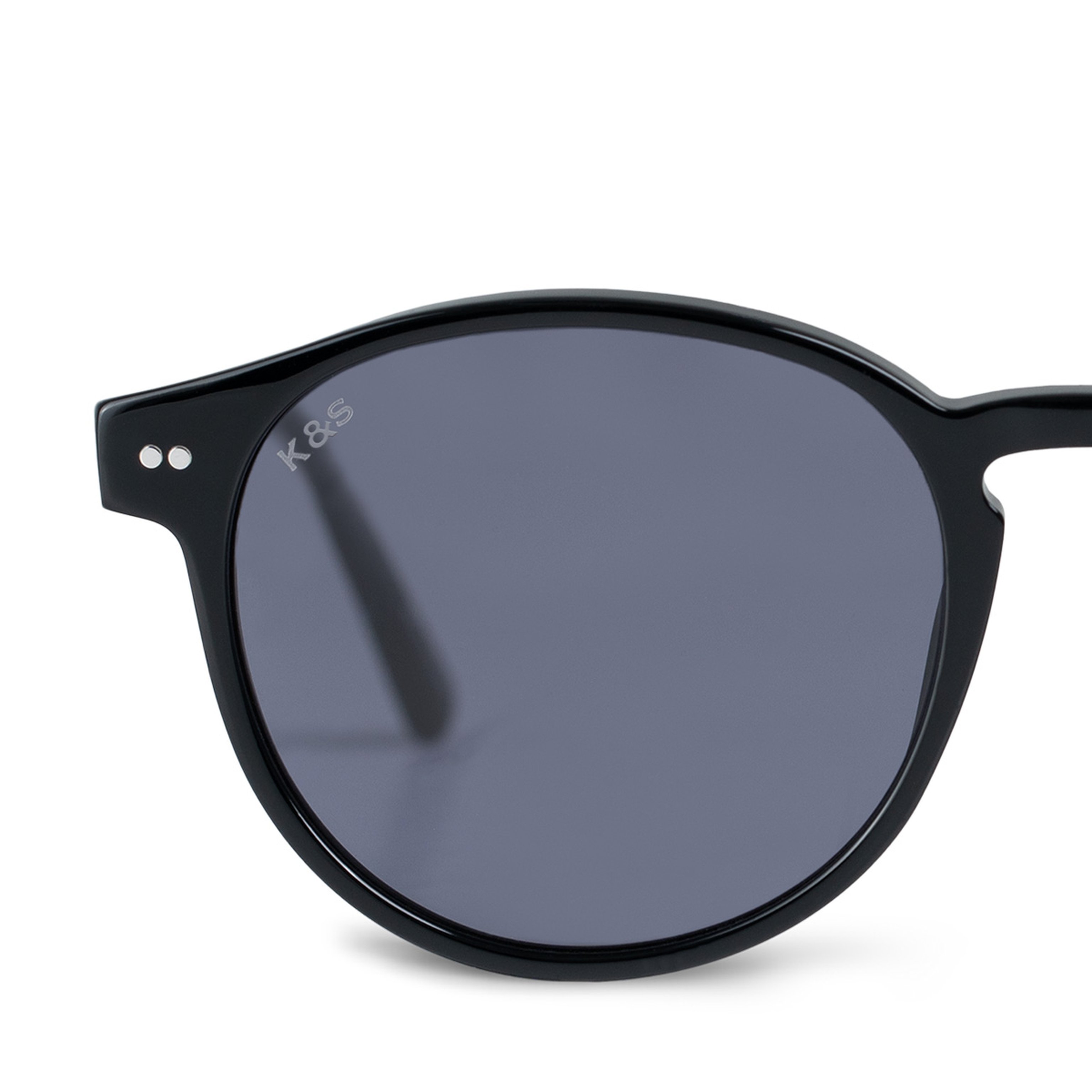 Close-up of stylish black sunglasses featuring round, dark-tinted lenses. The frame has a sleek design with a small logo and two silver accents.