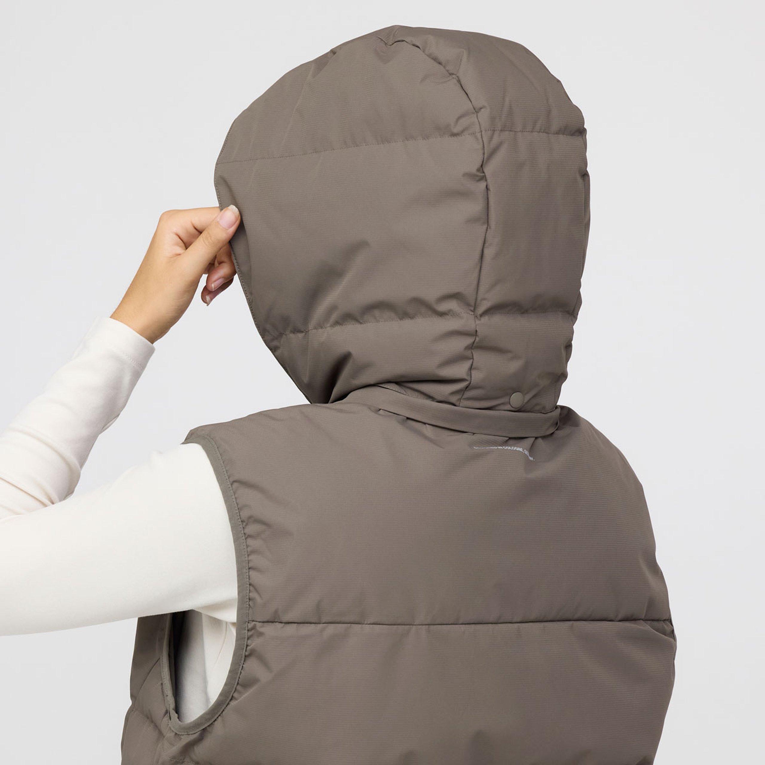 Nahaufnahme einer von hinten sichtbaren Person mit einer wattierten Weste mit Kapuze, die mit einer Hand die Kapuze richtet.