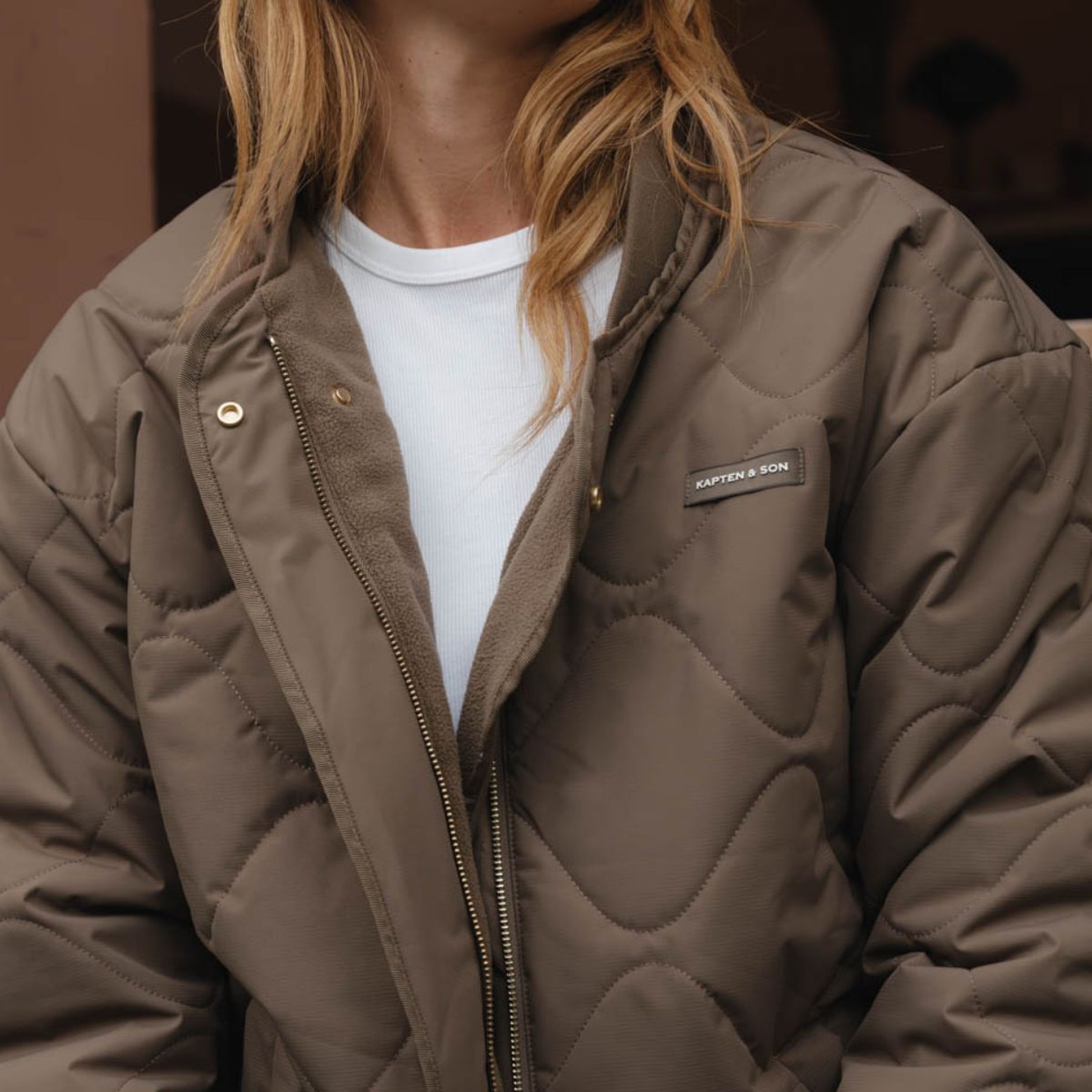 Nahaufnahme der gesteppten Jacke mit Frontreißverschluss und Zipper mit Markenlogo