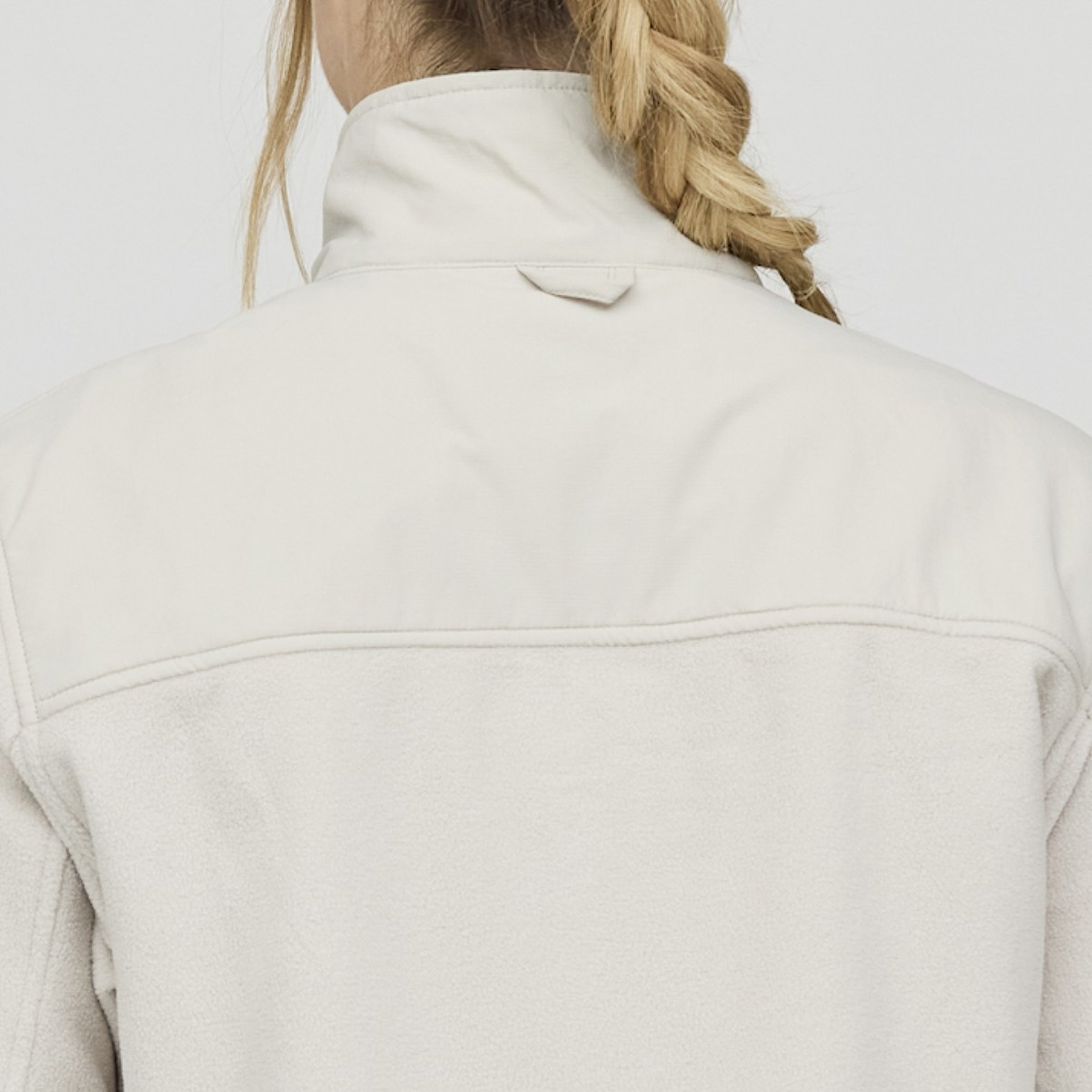 Vista posteriore di una persona con capelli biondi intrecciati, che indossa una giacca in pile color crema chiaro. L'immagine trasmette una sensazione di calore e comfort.