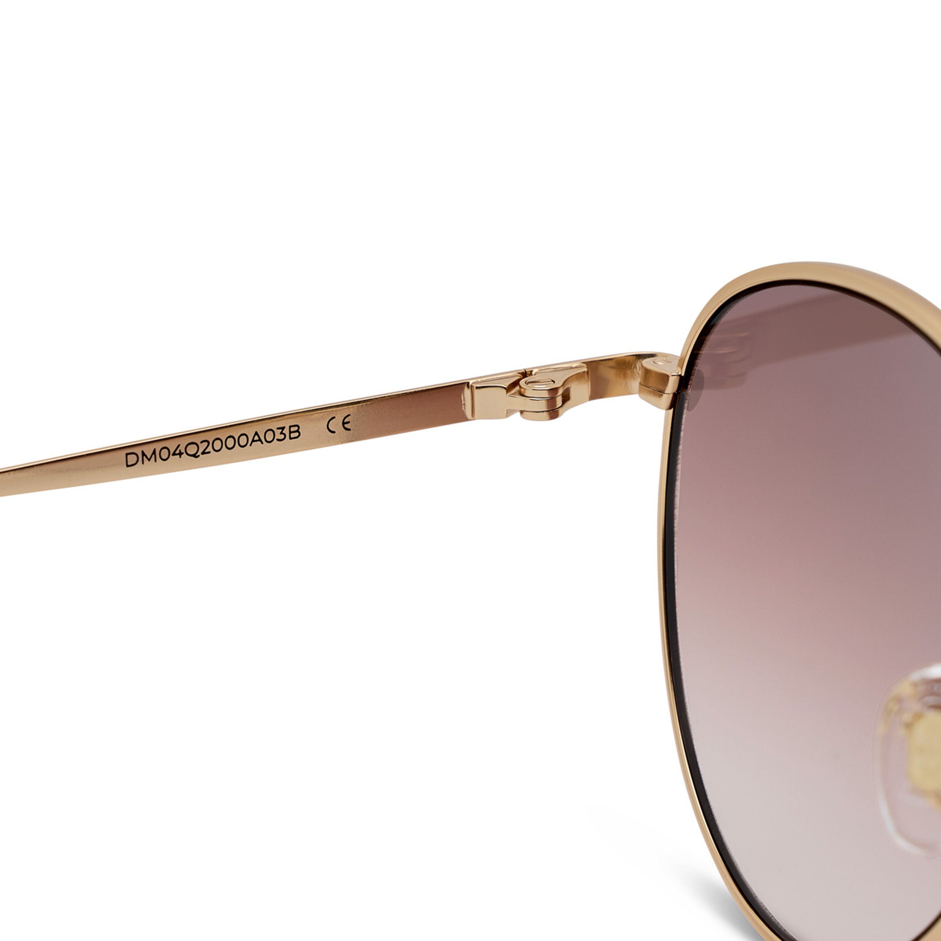 Close-up of brown sunglasses showing the arm with engraved details and a gold hinge. The lens has a gradient tint, adding a stylish touch.