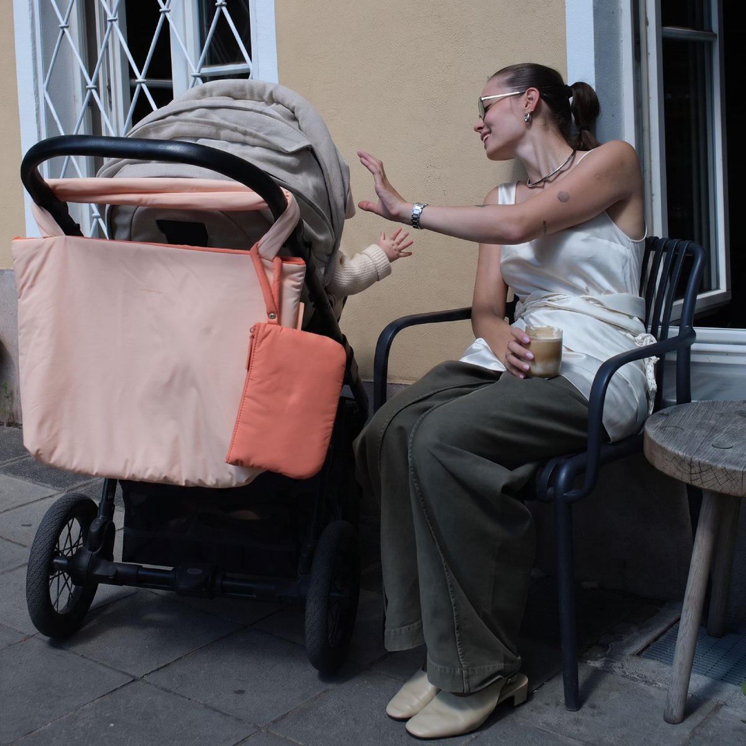 frau schiebt kinderwagen mit rosa wickeltasche dran