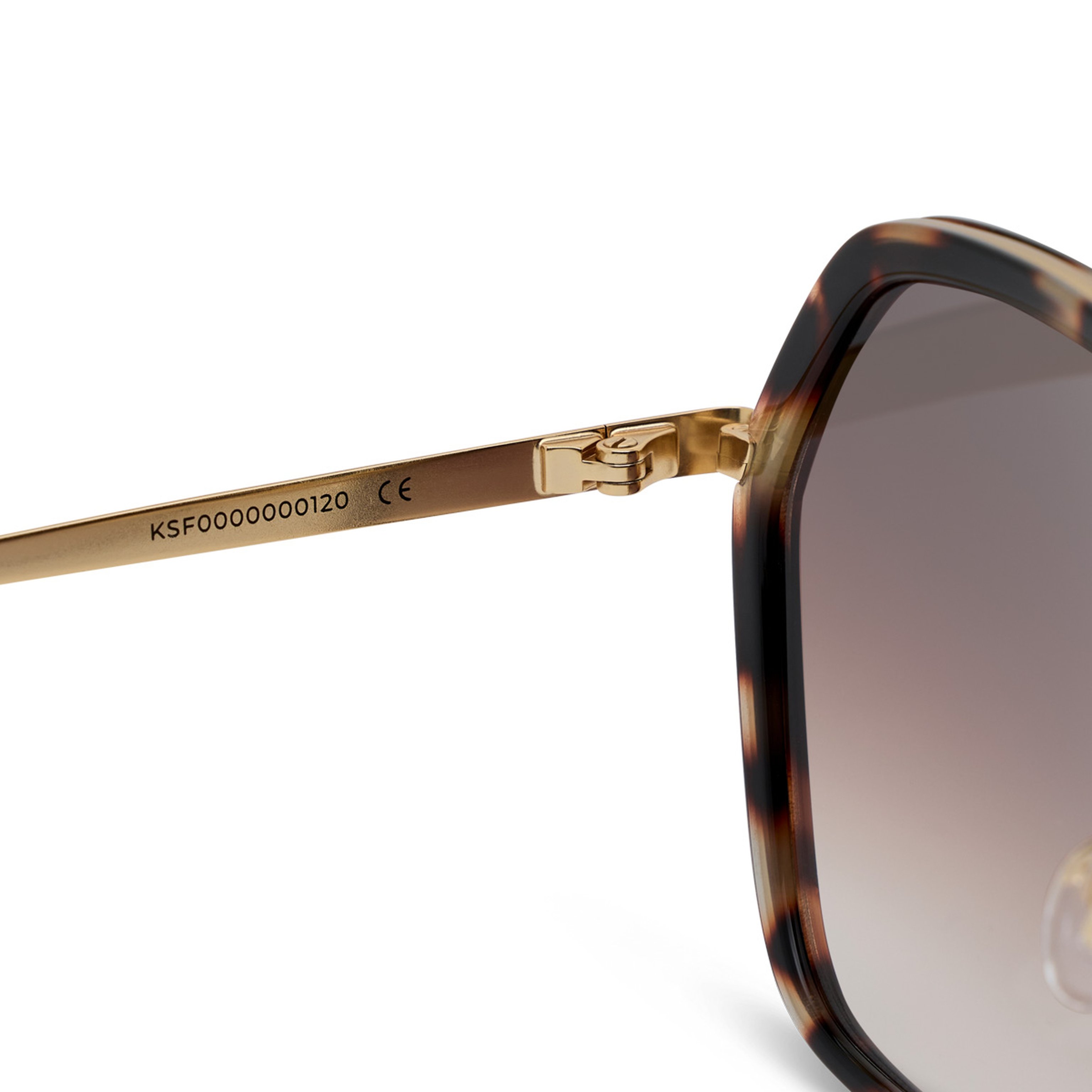 Close-up of brown sunglasses showing the arm with engraved details and a gold hinge. The lens has a gradient tint, adding a stylish touch.