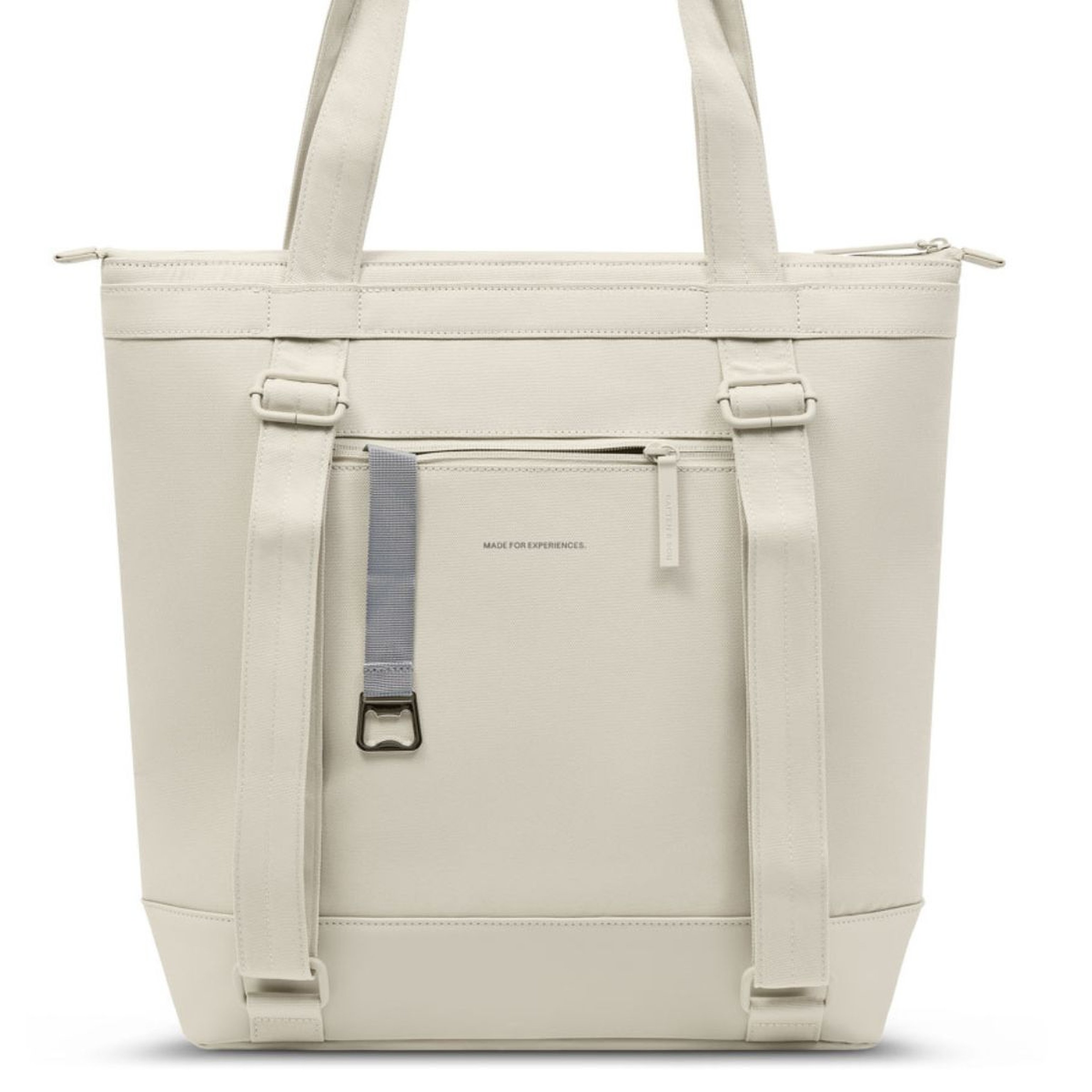 Cream-colored tote bag with sturdy handles, front zip pocket, and a gray strap with a metal buckle. The design is minimalist and practical.