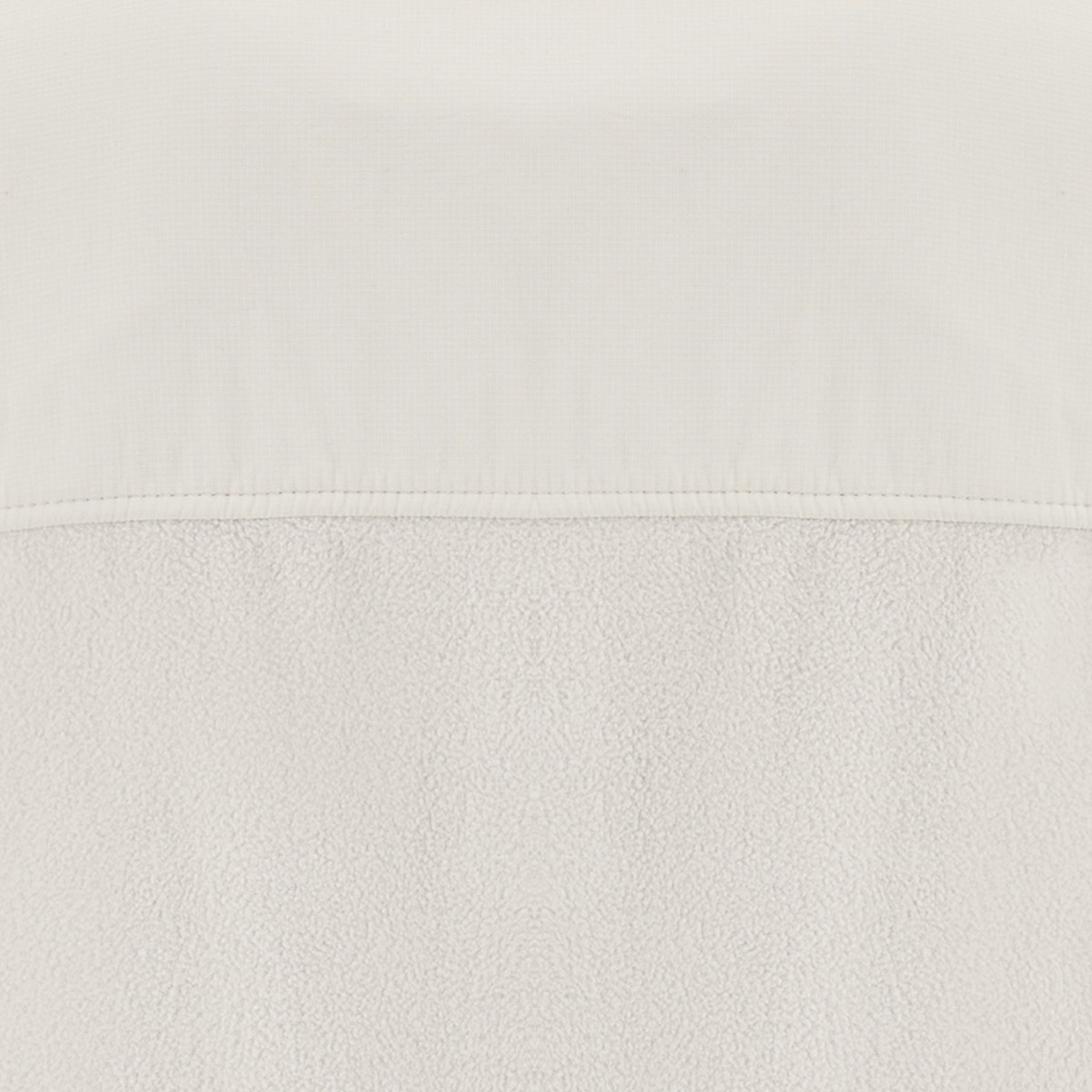 Primo piano di un tessuto bianco strutturato con una sezione liscia sopra un'area morbida simile al pile. La semplicità trasmette una sensazione accogliente e minimalista.