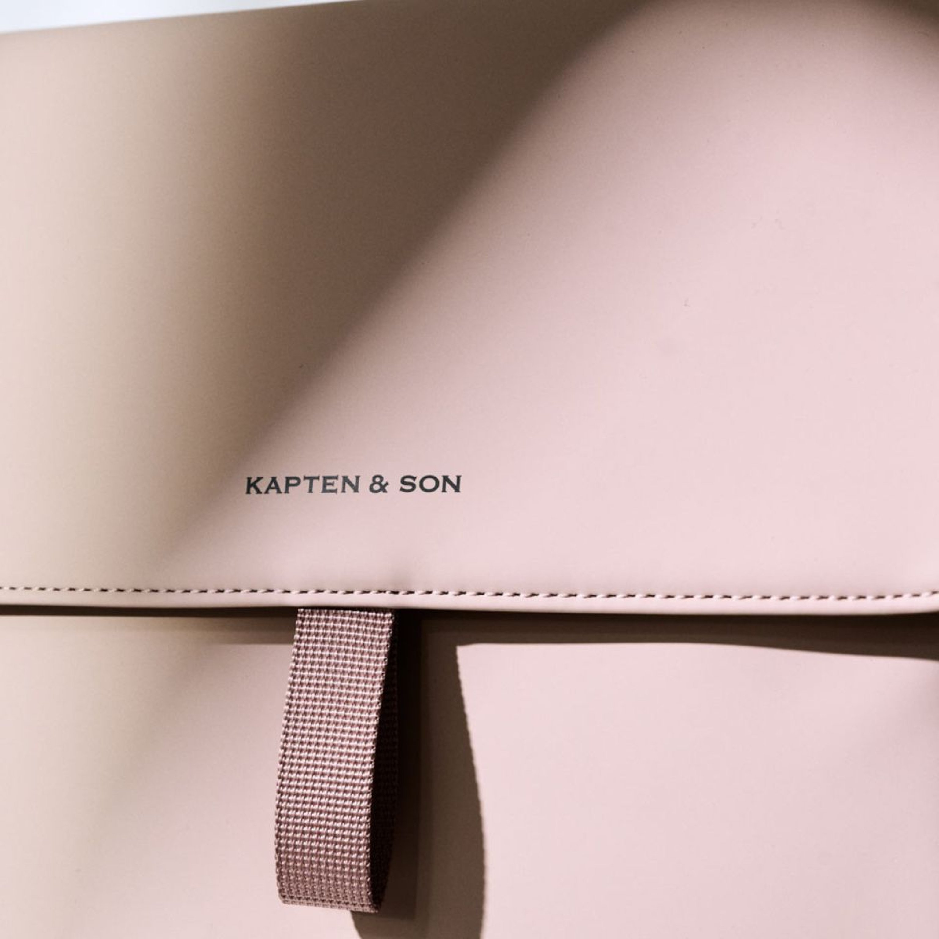 A pink backpack featuring the name "Kapten and Son" prominently displayed on its surface.