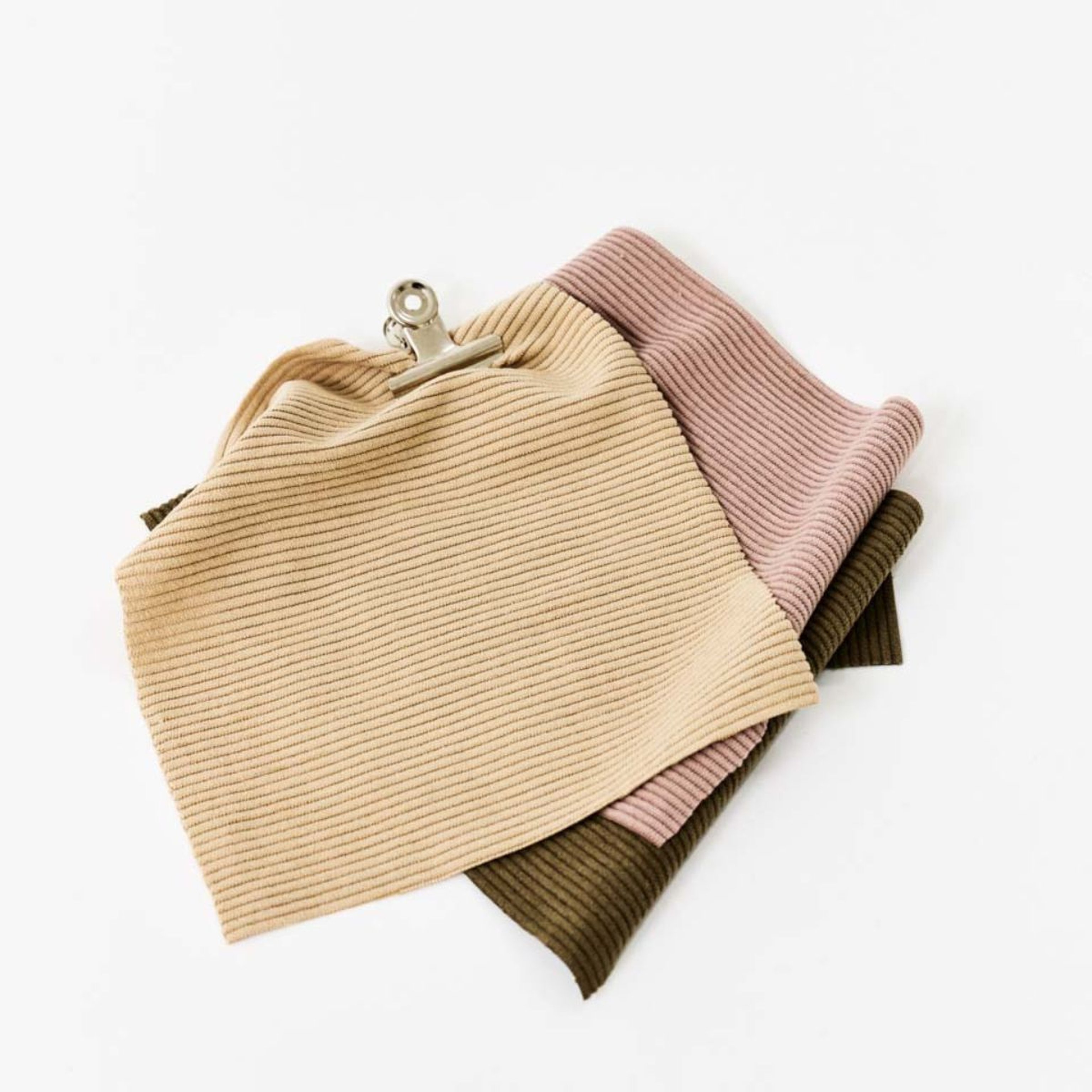Three corduroy fabrics in beige, light pink, and olive, with a metallic clip for fastening.