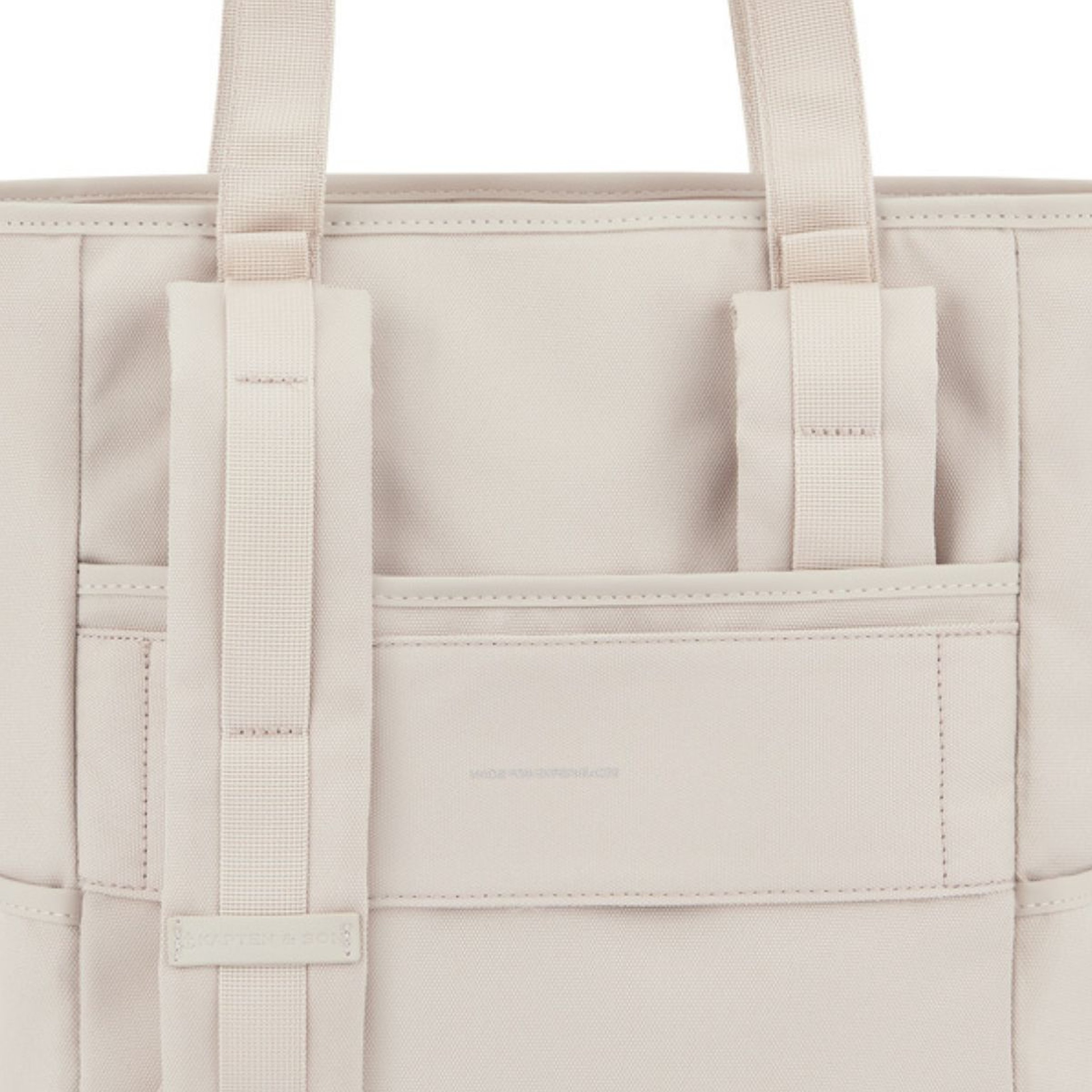 Nahaufnahme einer beige Stofftasche mit zwei Henkeln und einer Vorderseite-Tasche. Das minimalistische, klare Design vermittelt Eleganz und Schlichtheit.