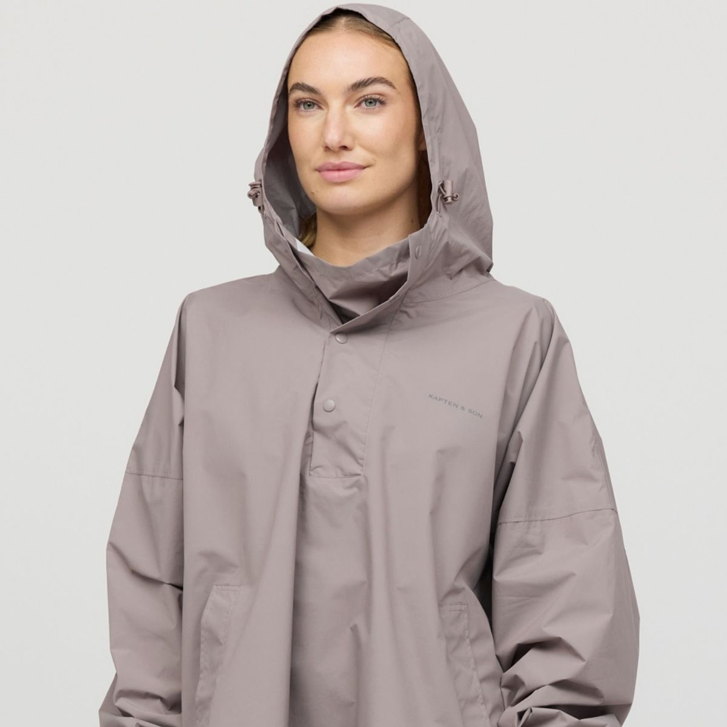 A person wearing a hooded raincoat stands against a plain background, exuding a calm and confident demeanor.