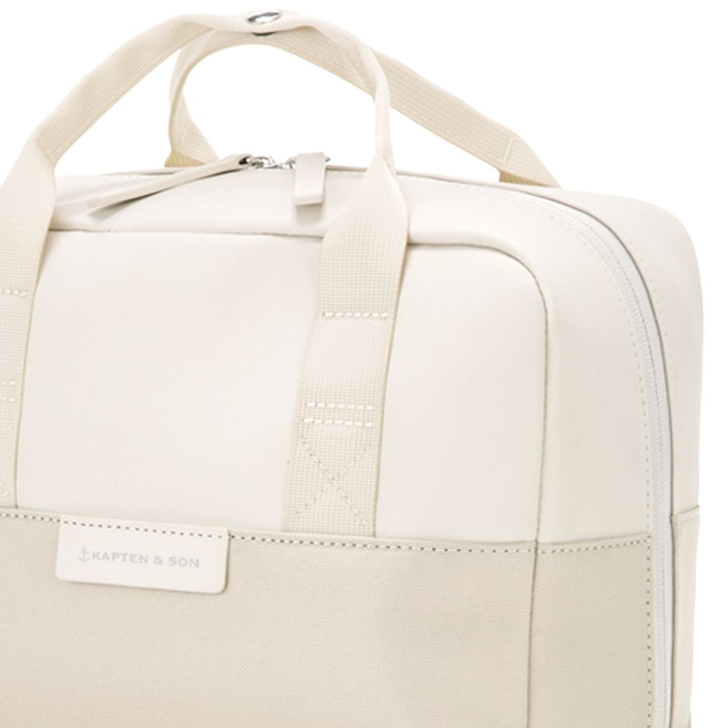 Cream-colored Kapten & Son bag close-up, featuring sturdy handles and a prominent zipper. Minimalistic design with a modern and elegant tone.