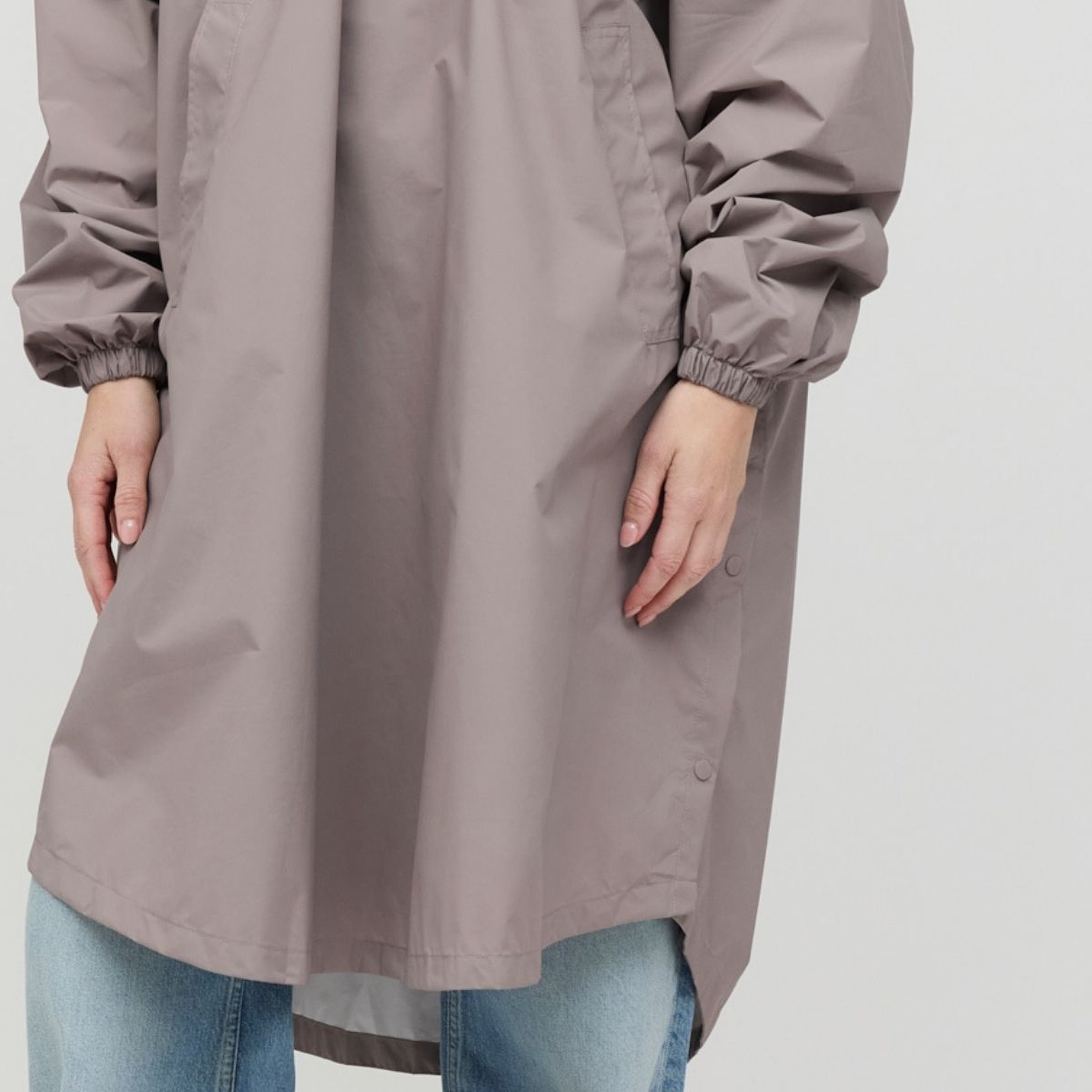 A person wearing a long raincoat with elastic cuffs, paired with light blue jeans. The raincoat has a relaxed fit and covers most of the jeans.