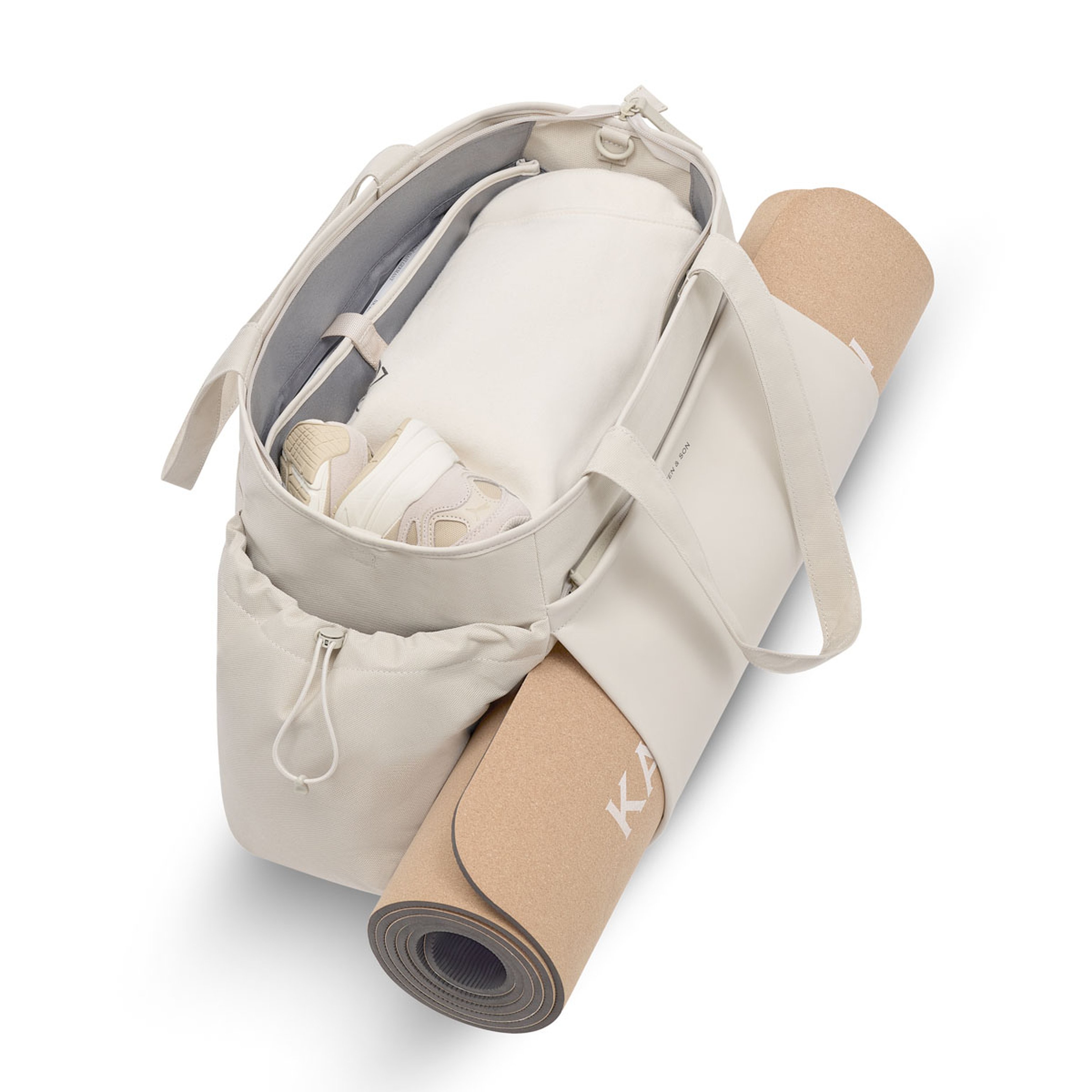 Offene Sporttasche in Beige mit seitlich befestigter Yogamatte; im Innenraum sind Sneakers und weitere helle Kleidungsstücke organisiert verstaut.